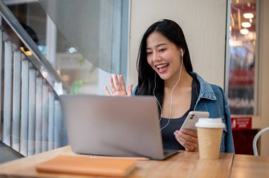 Kot ceketli çekici bir Asyalı kadın bir kahve dükkanında çalışıyor ve ekibiyle çevrimiçi bir toplantı yapıyor. Modern yaşam tarzları, kablosuz teknoloji