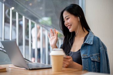 Kot ceketli çekici bir Asyalı kadın bir kahve dükkanında çalışıyor ve ekibiyle çevrimiçi bir toplantı yapıyor. Modern yaşam tarzları, kablosuz teknoloji