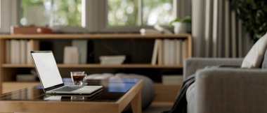 Çağdaş oturma odasındaki kahve masasının üzerinde beyaz ekran maketi ve kahve fincanı olan bir dizüstü bilgisayarın yan görüntüsü. ev çalışma alanı, 3d görüntüleme, 3d illüstrasyon