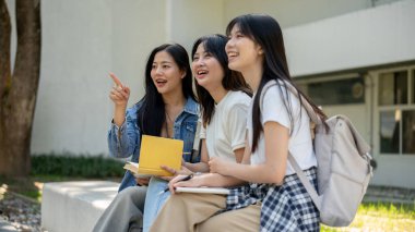 Bir grup neşeli Asyalı kız üniversite öğrencisi, en iyi arkadaşlar, kolej parklarında birlikte oturuyorlar, sohbet ediyorlar ve birlikte bir şeyler izliyorlar..