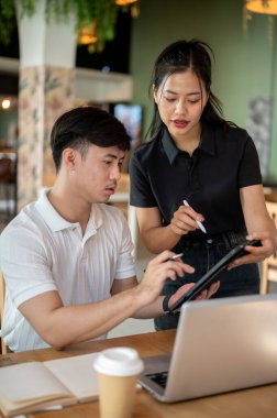 İki odaklanmış Asyalı meslektaşı, bir erkek ve bir kadın, tablet ekranına bakıyor, içeriğini tartışıyor, beyin fırtınası yapıyor ve bir proje hakkındaki fikirlerini paylaşıyorlar..