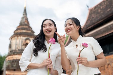 Geleneksel Kuzey Tayland-Lanna elbiseli iki güzel, gülümseyen Asyalı kadın bir tapınakta duruyorlar, pembe nilüferler tutuyorlar ve sohbet ediyorlar. Budist, Tayland kültürü