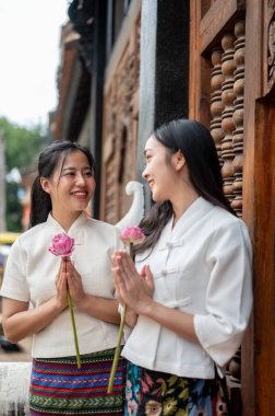 Geleneksel Thai-Lanna elbiseli iki güzel Asyalı kadın tapınakta duruyor, dua pozisyonu almış birbirlerine gülümsüyorlar. Tayland kültürü, Budist