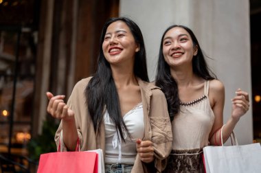 Moda kıyafetleri içinde iki güzel ve mutlu Asyalı kadın alışveriş torbalarıyla mağazadan çıkıp hafta sonu alışveriş çılgınlığının tadını çıkarıyorlar. şehir hayatı, seyahat, alışveriş, yaşam tarzları