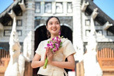 Geleneksel Kuzey Tayland-Lanna elbiseli güzel, gülümseyen Asyalı bir kadın bir tapınakta duruyor, ellerinde dua eden bir duruşta çiçekleri tutuyor ve başka tarafa bakıyor. Budist, Tayland kültürü, bir dilek tut.