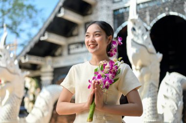 Geleneksel Kuzey Tayland-Lanna elbiseli güzel, gülümseyen Asyalı bir kadın bir tapınakta duruyor, ellerinde dua eden bir duruşta çiçekleri tutuyor ve başka tarafa bakıyor. Budist, Tayland kültürü, bir dilek tut.