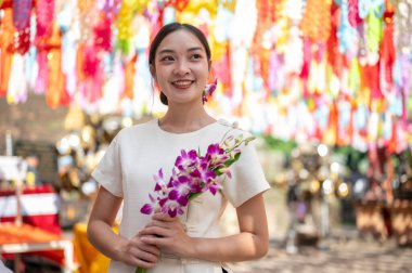 Geleneksel Kuzey Tayland elbisesi giymiş çekici, gülümseyen Asyalı bir kadın elinde renkli fenerlerle bir buket orkide ile tapınakta duruyor. Loy Krathong festivali, Tayland kültürü