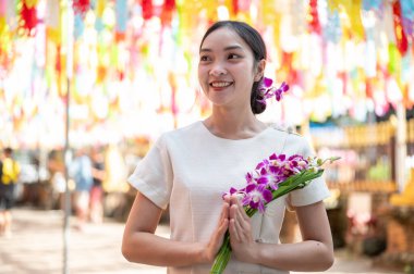 Geleneksel Kuzey Tayland elbisesi giymiş çekici, gülümseyen Asyalı bir kadın elinde renkli fenerlerle bir buket orkide ile tapınakta duruyor. Loy Krathong festivali, Tayland kültürü