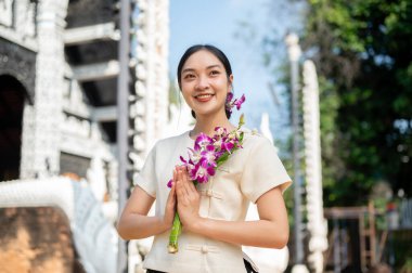 Geleneksel Tayland Lanna elbisesi giymiş çekici bir Asyalı kadın güzel bir tapınağın önünde duruyor elinde dua eden bir vaziyette, kameradan uzağa bakıyor. Tayland Kültür Seyahati