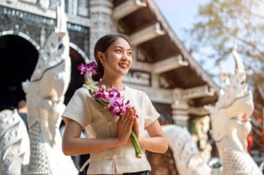 Geleneksel Tayland Lanna elbisesi giymiş çekici bir Asyalı kadın güzel bir tapınağın önünde duruyor elinde dua eden bir vaziyette, kameradan uzağa bakıyor. Tayland Kültür Seyahati