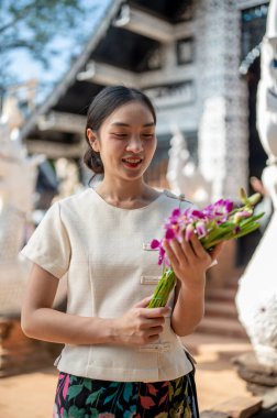 Geleneksel Tayland Lanna elbisesi giymiş çekici bir Asyalı kadın tapınağın dışında dururken elindeki güzel orkide buketine hayran kalıyor. Budizm, Tayland, kültür