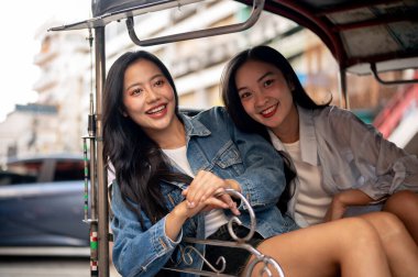İki mutlu, çekici Asyalı genç kız Tayland 'da bir tuk-tuk' la gezintisinin tadını çıkarıyorlar. Yazın Güneydoğu Asya 'yı geziyorlar ve kameraya gülümsüyorlar. Turist, seyahat, ulaşım, Tayland