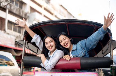 İki güzel ve neşeli Asyalı kız turist şehri keşfetmekten ve Tayland 'da römorkörle gezmekten zevk alıyor, kameraya gülümsüyorlar. Güneydoğu Asya seyahati, tatil, yaz gezisi, Tayland