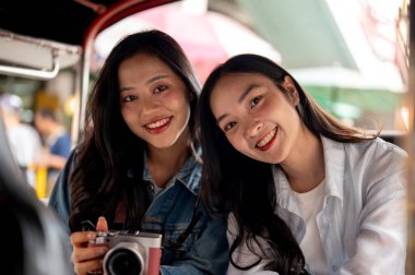 İki mutlu, çekici Asyalı genç kız Tayland 'da bir tuk-tuk' la gezintisinin tadını çıkarıyorlar. Yazın Güneydoğu Asya 'yı geziyorlar ve kameraya gülümsüyorlar. Turist, seyahat, ulaşım, Tayland