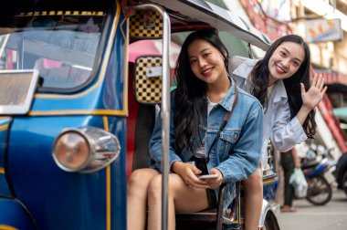 İki güzel ve neşeli Asyalı kadın, yaz tatillerinde birlikte seyahat ederken şehrin çarpıcı manzarasından heyecan duyarak Tayland 'da tuk-tuk turunun tadını çıkarıyorlar..