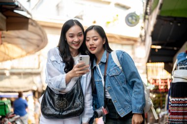 İki heyecanlı, neşeli Asyalı bayan arkadaş yerel bir pazarı birlikte keşfetmekten zevk alıyorlar, bir yeri araştırıyorlar, akıllı telefondan haritaya bakıyorlar, Güneydoğu Asya 'da eğleniyorlar.