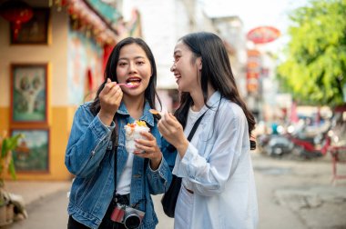 İki güzel, neşeli genç Asyalı bayan turist Tayland 'da bir markette sokak yemeklerinin tadını çıkarıyorlar, şehir keşifleri sırasında sokakta birlikte hindistan cevizli dondurma yiyorlar. Güneydoğu Asya