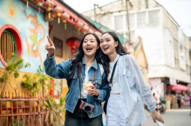 İki neşeli genç Asyalı bayan turist Tayland 'da şehri birlikte keşfediyor, cadde boyunca yürürken sokak yemeklerinin tadını çıkarıyor, bir binayı işaret ederek yerlerini tespit ediyorlar..