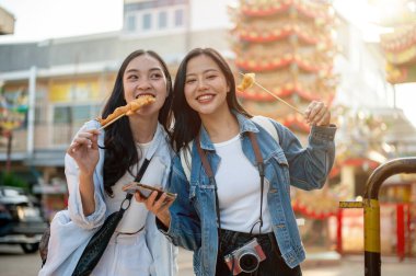 İki güzel, neşeli Asyalı genç bayan turistin portresi güneşli bir günde şehri keşfederken Tayland 'da sokak yemeklerinin tadını çıkarıyor. Güneydoğu Asya, tatil, gezi, yaz tatili