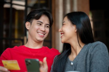 Hoş, genç bir Asyalı çift, rahat ve sıcak giysiler içinde bir kafede rahatlatıcı bir anın tadını çıkarıyor, akıllı telefondan internetten alışveriş yapıyorlar. İnsanlar, yaşam tarzları, nakitsiz hayat, e-ticaret