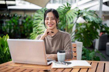 Sakin bir kafeden uzaktan çalışan çekici bir Asyalı kadın dışarıda bir masada dizüstü bilgisayarıyla oturuyor ve kameraya gülümsüyor. İnsanlar, kablosuz teknoloji ve yaşam tarzları