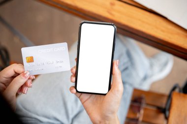 Kafede otururken elinde kredi kartı ve akıllı telefon tutan bir kadının yakın çekimi. Beyaz ekran maketli akıllı telefon. çevrimiçi ödeme, mobil bankacılık, çevrimiçi alışveriş, tasarruf, mali