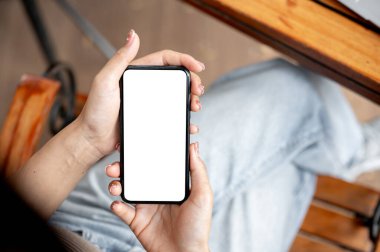 Bir kafede otururken akıllı telefonunu kullanan bir kadının yakın çekimi. Beyaz ekran maketli akıllı telefon. İnsanlar ve kablosuz teknoloji kavramları