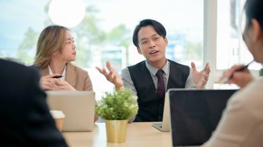 Resmi takım elbiseli profesyonel, zeki bir Asyalı işadamı, modern bir ofis ortamında yaptığı ortak bir iş toplantısında kendi fikirlerini paylaşıyor ve ekibine projesini anlatıyor..