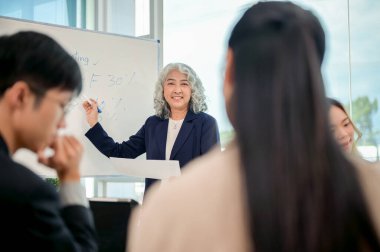 Profesyonel bir Asyalı kıdemli CEO, pazarlama ekibiyle modern bir toplantı odasında yaptığı toplantıda yeni projenin pazarlama stratejilerini tartışıyor ve fikir alışverişinde bulunuyor..