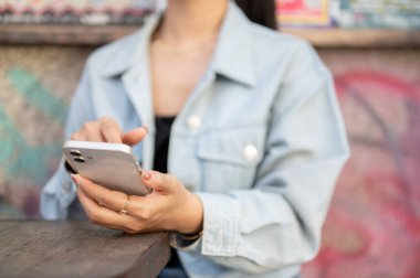 Kot ceketli bir kadının yakın plan fotoğrafı şehirdeki bir kafenin açık masasında oturuyor, akıllı telefonunu kullanıyor, kısa mesajlar okuyor. İnsanlar, yaşam tarzları, kablosuz teknoloji