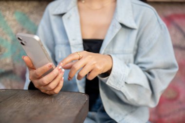 Kot ceketli bir kadının yakın plan fotoğrafı şehirdeki bir kafenin açık masasında oturuyor, akıllı telefonunu kullanıyor, kısa mesajlar okuyor. İnsanlar, yaşam tarzları, kablosuz teknoloji