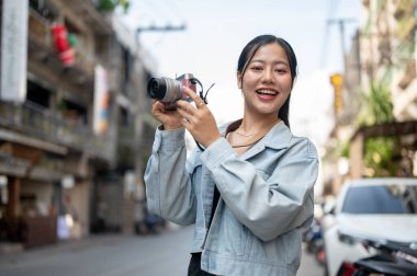 Kot ceketli, çekici, mutlu bir Asyalı kadın turist kamerasıyla fotoğraf çekerken kameraya gülümsüyor. insanlar ve yaşam tarzı kavramları