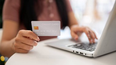 Bilgisayarını kullanırken kredi kartını kameraya gösteren kapalı bir masadaki dizüstü bilgisayarın klavyesinde yazan bir kadın. Online alışveriş, alışveriş sitesi, online ödeme, e-ticaret