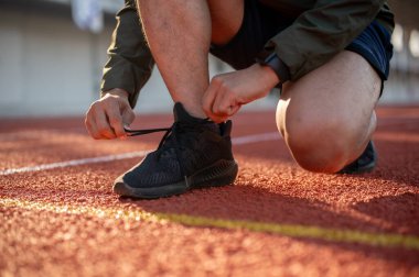 Güçlü, atletik bir erkek koşucunun yakın plan çekimi. Koşu ayakkabılarını bağlıyor, sabahları stadyumda koşmaya hazırlanıyor..
