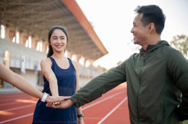 Bir grup neşeli Asyalı koşucu sabah stadyumda koşmadan önce cesaretlendirmek için ellerini bir araya getiriyorlar. dostluk, spor, yaşam tarzları