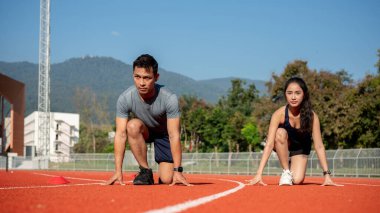 Güneşli bir günde bir stadyumdaki yarış pistinde yarışmaya hazır iki kararlı Asyalı koşucu başlangıç pozisyonunda. Koşu, antrenman, insanlar ve spor