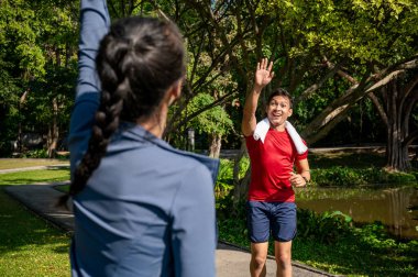 Neşeli, gülümseyen Asyalı bir adam spor giyim kuşamında arkadaşlarıyla selamlaşır ve güneşli bir günde parkta koşarken birbirlerine çarparlar. insanlar ve yaşam tarzları kavramları