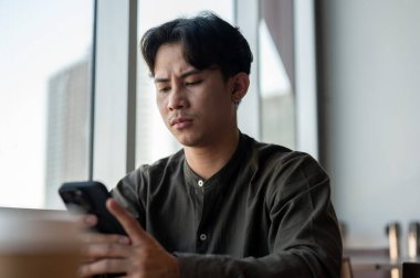 Ciddi bir Asyalı adam, modern bir kafede oturmuş sevgilisiyle mesajlaşırken ya da uygulamadan şikayet ederken akıllı telefonuyla mesaj atıyor..