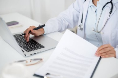 Ofisteki masasında çalışan, klavyesini dizüstü bilgisayarında yazan bir kadın doktorun yakın plan fotoğrafı. sağlık hizmeti kavramı