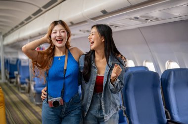İki neşeli, çekici Asyalı bayan arkadaş, yaz tatilleri için heyecanlılar, mutlu yüz ifadeleriyle bir koridorda duruyorlar, neşeyle gülüyorlar. uçak, ulaşım, tatil, yaşam tarzı
