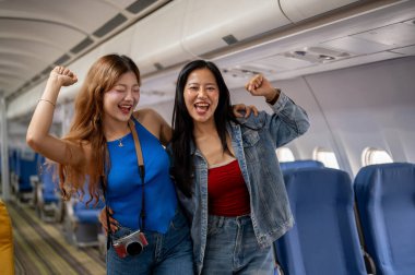 İki heyecanlı, neşeli Asyalı bayan en iyi arkadaş yaz tatilleri için heyecanlı bir şekilde kameraya gülümseyen bir şekilde uçağın koridorunda duruyorlar..