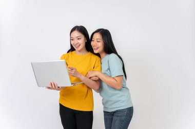 İki mutlu, güzel Asyalı bayan arkadaş izole edilmiş beyaz bir arka planda dizüstü bilgisayardan bir şeye bakıyorlar. İnternetten ders çalışmak, internetten alışveriş yapmak, film izlemek.