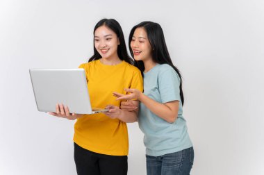 İki mutlu, güzel Asyalı bayan arkadaş izole edilmiş beyaz bir arka planda dizüstü bilgisayardan bir şeye bakıyorlar. İnternetten ders çalışmak, internetten alışveriş yapmak, film izlemek.
