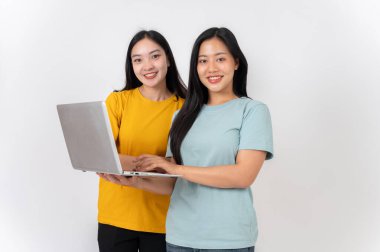 Dizüstü bilgisayarı olan iki mutlu Asyalı kadın beyaz bir stüdyonun arka planında kameraya gülümsüyor. insanlar ve teknoloji kavramları