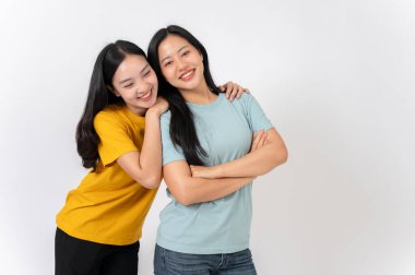 İki sevimli, gülümseyen Asyalı kadın beyaz bir stüdyonun arka planında dikilirken sarılıyorlar. en iyi arkadaş, arkadaşlık, ilişki, üniversite öğrencisi