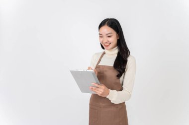 Kahverengi önlüklü, gülümseyen Asyalı bir bayan garson ya da kahve dükkanı çalışanı dijital tabletine beyaz bir stüdyo arka planına karşı durarak sipariş yazar. Küçük işletme, işletme sahibi, işçi