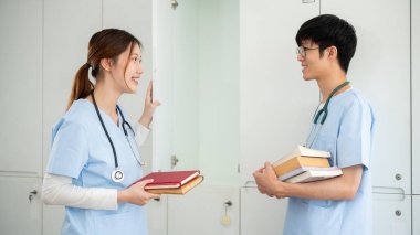 İki mutlu, gülümseyen Asyalı erkek ve bayan tıp öğrencisi soyunma odasındaki bir dolaptan ders kitaplarını alıp derse girmeye hazırlanırken konuşuyorlar. Tıp fakültesi, doktor, hastane.