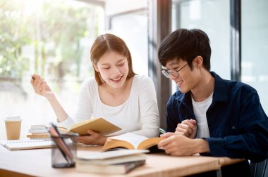 İki genç Asyalı üniversite öğrencisi bir kafede ya da kampüs kütüphanesinde bir kitaptan bir konuyu tartışarak birlikte bir sınava hazırlanıyorlar. insanlar ve eğitim kavramları