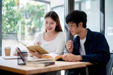 İki genç Asyalı üniversite öğrencisi bir kafede ya da kampüs kütüphanesinde bir kitaptan bir konuyu tartışarak birlikte bir sınava hazırlanıyorlar. insanlar ve eğitim kavramları