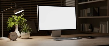 Masa lambasıyla aydınlatılan, gece odasındaki ahşap bir masanın üzerinde beyaz ekran maketi olan bir bilgisayarın yakın çekimi. Ofis, çalışma alanı, iş yeri, ev ofisi, 3D resim, 3D resim